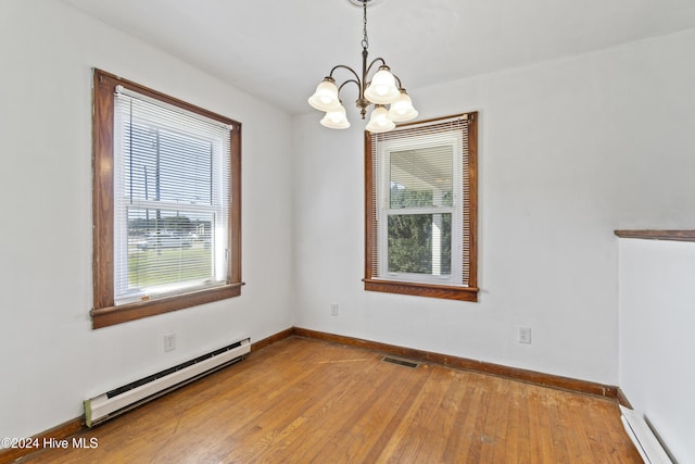 empty room with a baseboard heating unit, an inviting chandelier, and light hardwood / wood-style flooring