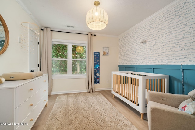 bedroom with light hardwood / wood-style flooring, ornamental molding, and a nursery area