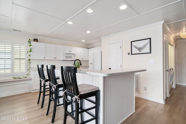 kitchen featuring an island with sink, white cabinets, a kitchen breakfast bar, ornamental molding, and white appliances