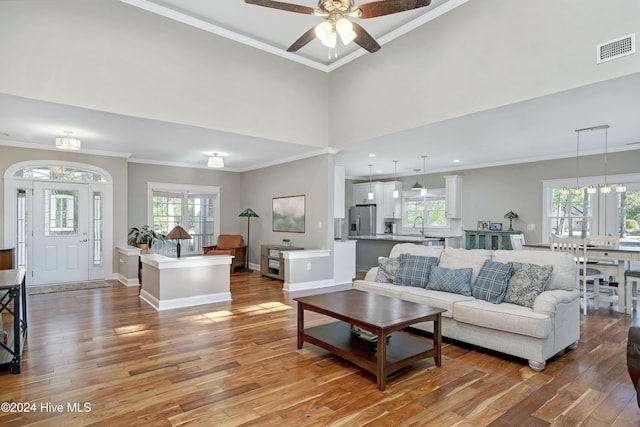 living room with ceiling fan with notable chandelier, light wood-type flooring, and crown molding