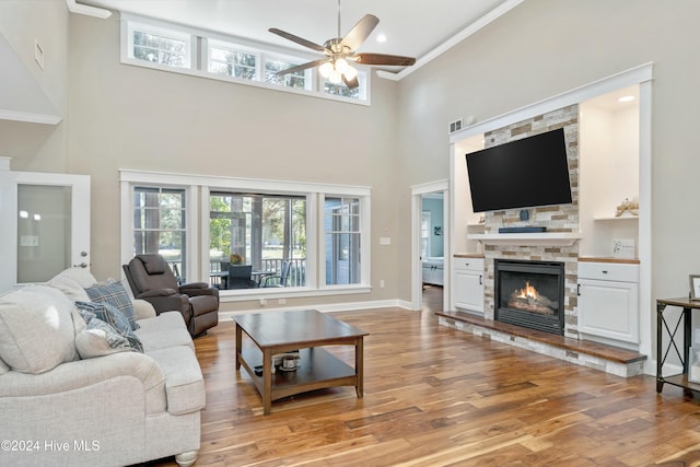 living room featuring a fireplace, a towering ceiling, a healthy amount of sunlight, and light wood-type flooring