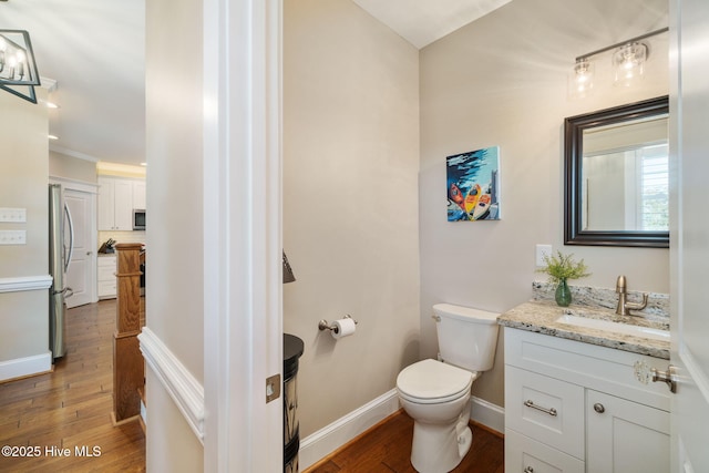 half bathroom featuring toilet, baseboards, wood finished floors, and vanity