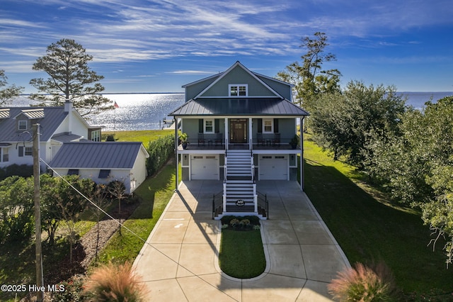coastal inspired home featuring a garage, concrete driveway, metal roof, a water view, and stairway