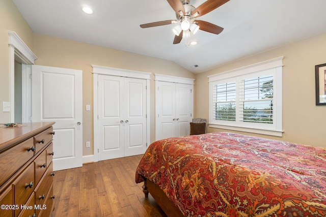 bedroom with recessed lighting, multiple closets, lofted ceiling, and hardwood / wood-style floors