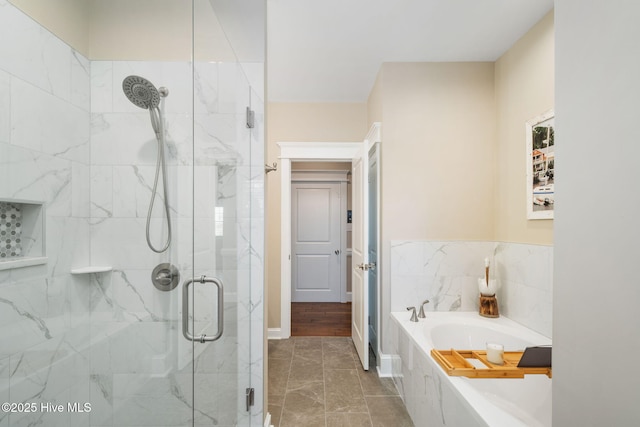 bathroom featuring marble finish floor, baseboards, a marble finish shower, and a garden tub