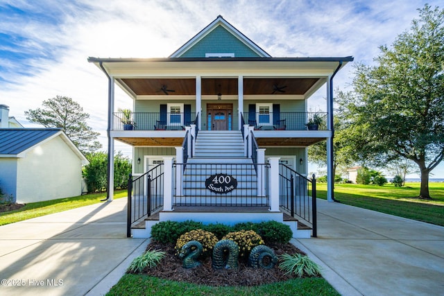 coastal home with a ceiling fan, covered porch, concrete driveway, and stairway