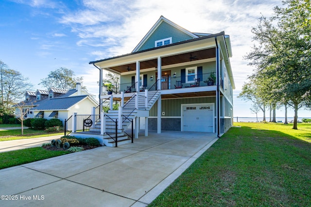 raised beach house featuring a front lawn, a garage, ceiling fan, stairway, and covered porch