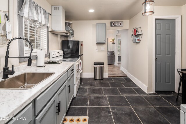 kitchen with dark tile patterned flooring, gray cabinets, white range, and sink