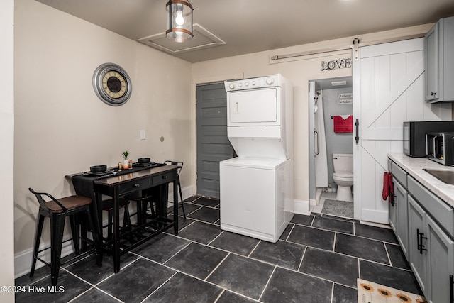 laundry room featuring a barn door, dark tile patterned floors, and stacked washer and clothes dryer