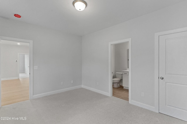 unfurnished bedroom featuring ensuite bath and light colored carpet