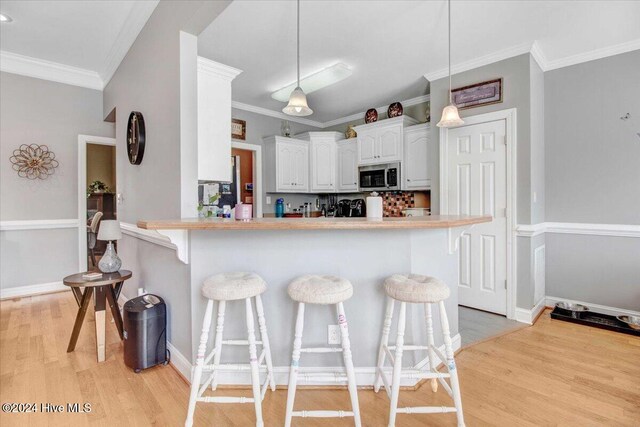 kitchen featuring kitchen peninsula, white cabinetry, hanging light fixtures, and a breakfast bar