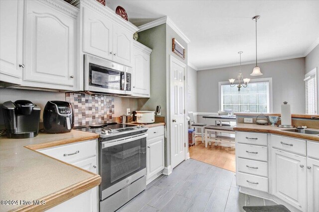 kitchen featuring ornamental molding, stainless steel appliances, light hardwood / wood-style floors, white cabinetry, and hanging light fixtures