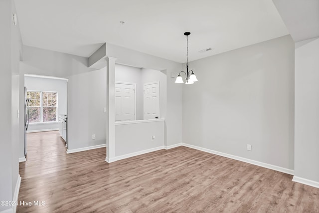 unfurnished dining area featuring decorative columns, a chandelier, and light wood-type flooring