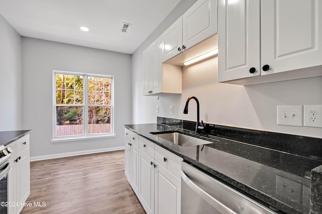 kitchen with light wood-type flooring, white cabinetry, dark stone counters, and sink