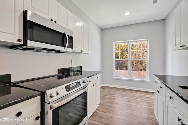 kitchen with dark stone countertops, white cabinetry, light hardwood / wood-style flooring, and appliances with stainless steel finishes