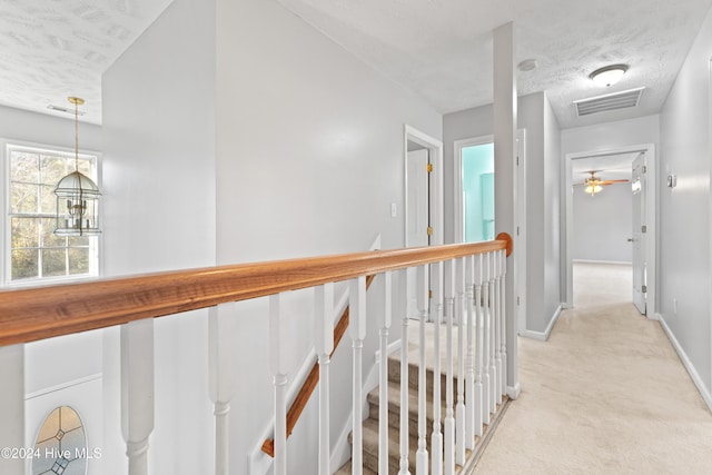 hallway with light colored carpet and a textured ceiling