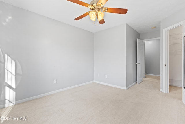 unfurnished bedroom featuring a walk in closet, a closet, light colored carpet, and ceiling fan