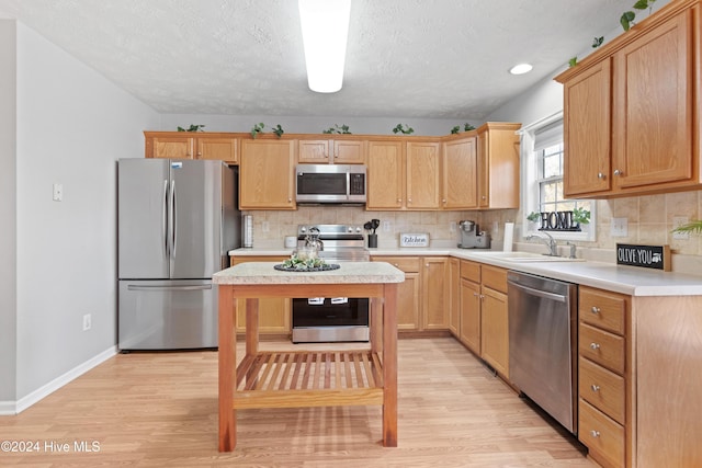 kitchen with a textured ceiling, sink, appliances with stainless steel finishes, and light hardwood / wood-style flooring