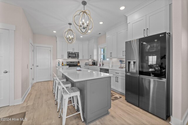 kitchen featuring stainless steel appliances, a kitchen island, light hardwood / wood-style flooring, pendant lighting, and white cabinets