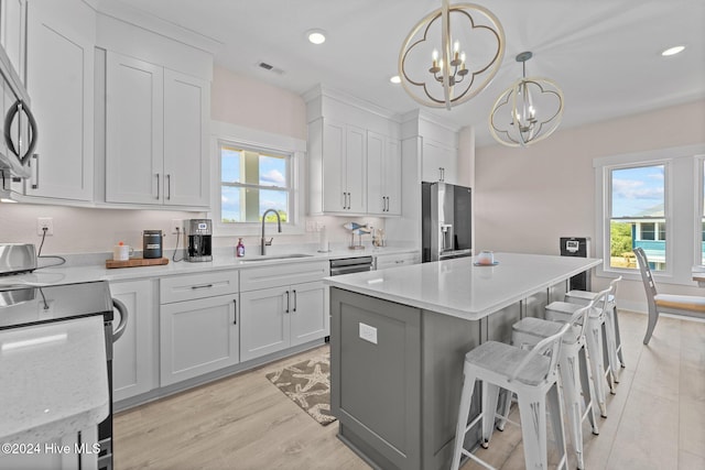 kitchen featuring a center island, white cabinets, sink, decorative light fixtures, and stainless steel appliances