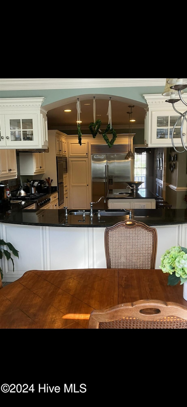 kitchen with built in refrigerator, hanging light fixtures, wall oven, and white cabinetry