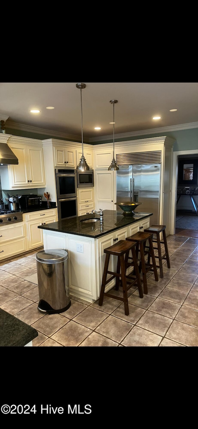 kitchen featuring decorative light fixtures, wall chimney exhaust hood, a kitchen bar, ornamental molding, and built in appliances