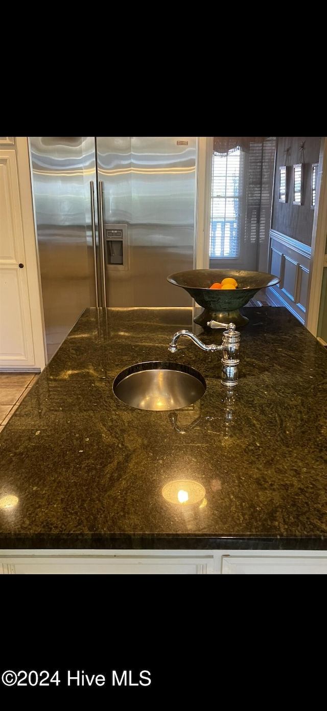 kitchen featuring sink, dark stone countertops, white cabinetry, and stainless steel fridge