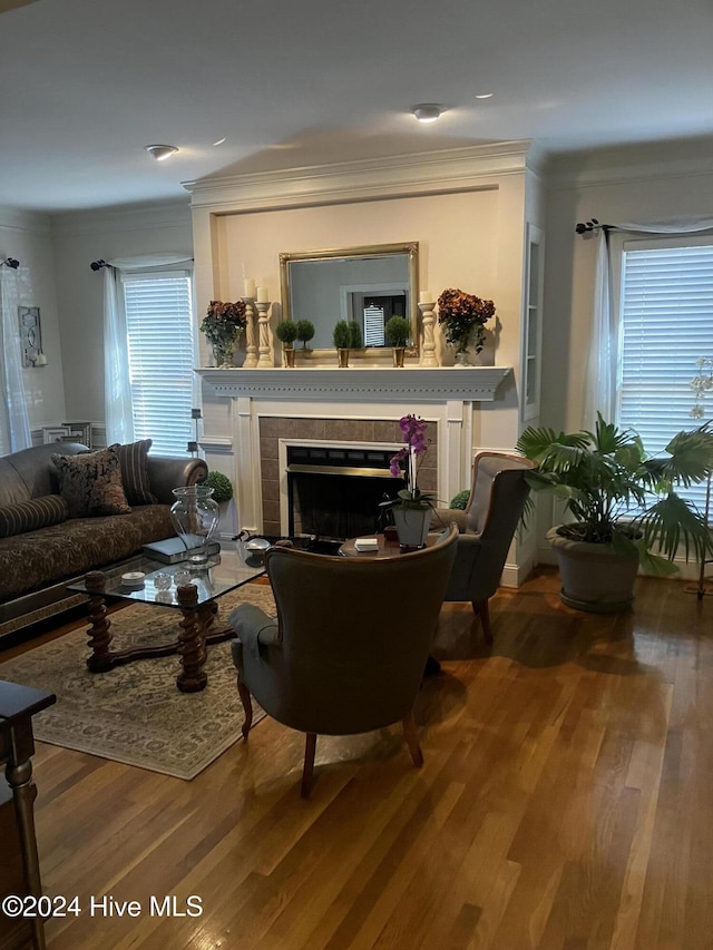 living room featuring wood-type flooring, a tiled fireplace, and crown molding