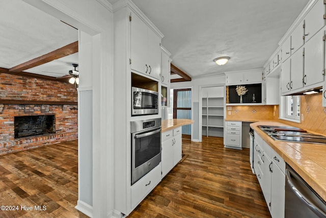 kitchen featuring a brick fireplace, stainless steel appliances, white cabinetry, and dark wood-type flooring