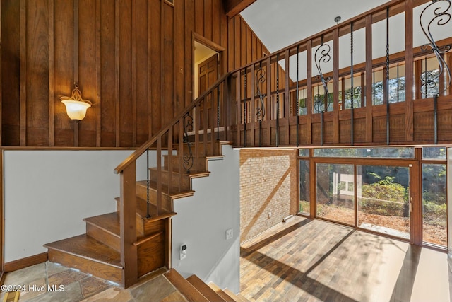 staircase with wooden walls and lofted ceiling with beams