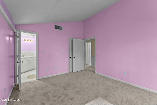 unfurnished bedroom with light colored carpet, lofted ceiling, and ensuite bath