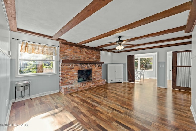 unfurnished living room with ceiling fan, a fireplace, beamed ceiling, and wood-type flooring