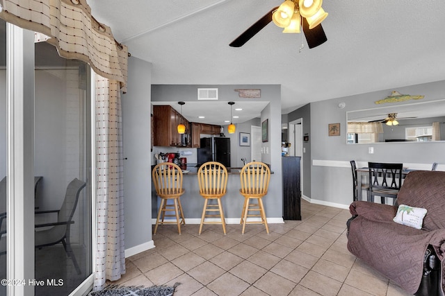 interior space with black fridge, a textured ceiling, ceiling fan, light tile patterned floors, and a breakfast bar area