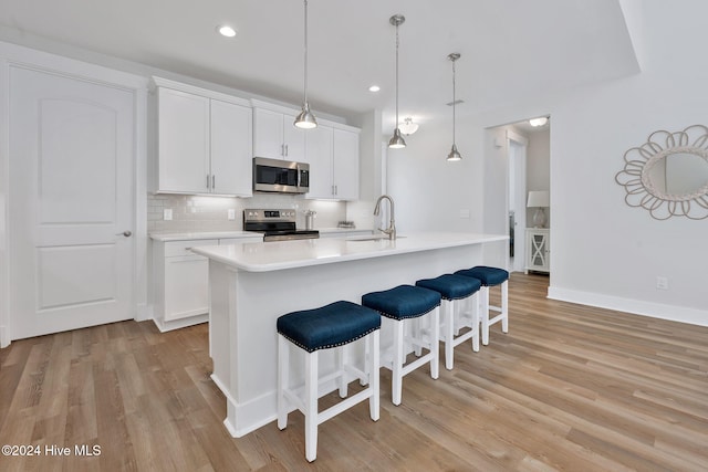 kitchen with white cabinets, light hardwood / wood-style flooring, stainless steel appliances, and an island with sink