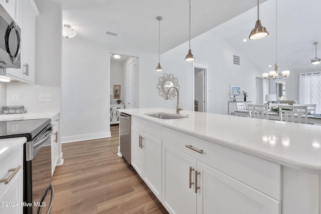 kitchen with stainless steel appliances, sink, pendant lighting, white cabinets, and lofted ceiling