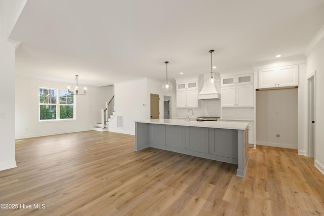 kitchen featuring premium range hood, white cabinetry, light hardwood / wood-style floors, a center island with sink, and tasteful backsplash