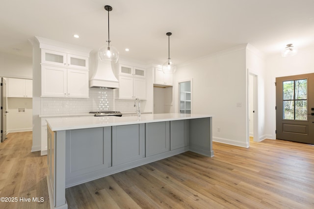 kitchen featuring white cabinetry, custom exhaust hood, decorative light fixtures, a kitchen island with sink, and crown molding