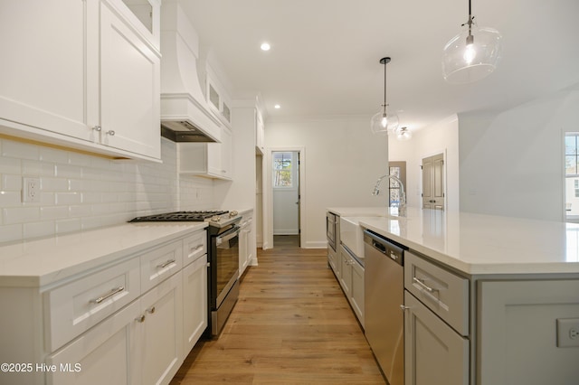 kitchen featuring decorative light fixtures, premium range hood, light wood-type flooring, appliances with stainless steel finishes, and white cabinets