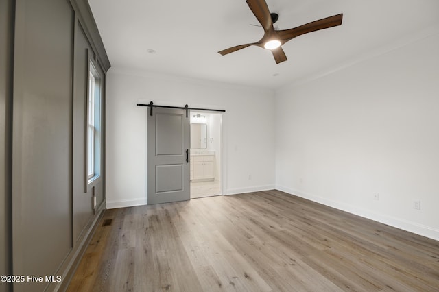 unfurnished bedroom featuring ceiling fan, a barn door, light hardwood / wood-style flooring, and multiple windows