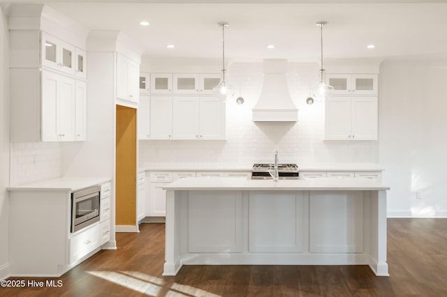 kitchen featuring white cabinetry, stainless steel appliances, hanging light fixtures, a kitchen island with sink, and custom range hood