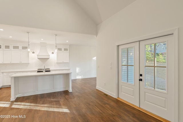 kitchen with white cabinetry, custom exhaust hood, backsplash, and an island with sink