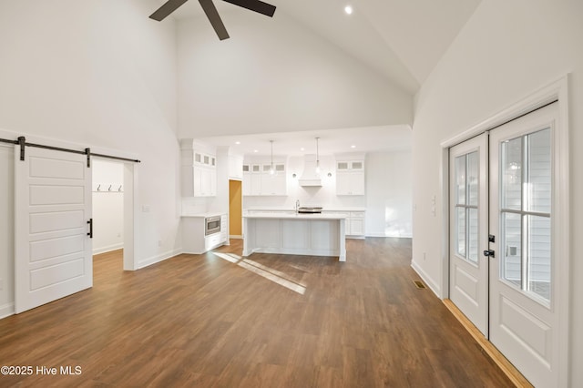 unfurnished living room featuring high vaulted ceiling, a barn door, ceiling fan, and dark hardwood / wood-style flooring