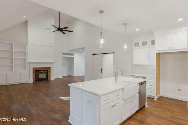 kitchen featuring white cabinetry, a barn door, a center island with sink, stainless steel dishwasher, and sink