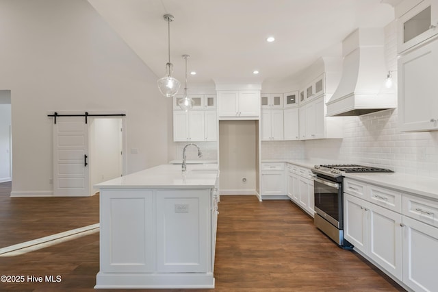 kitchen with a barn door, premium range hood, sink, stainless steel range with gas stovetop, and a kitchen island with sink