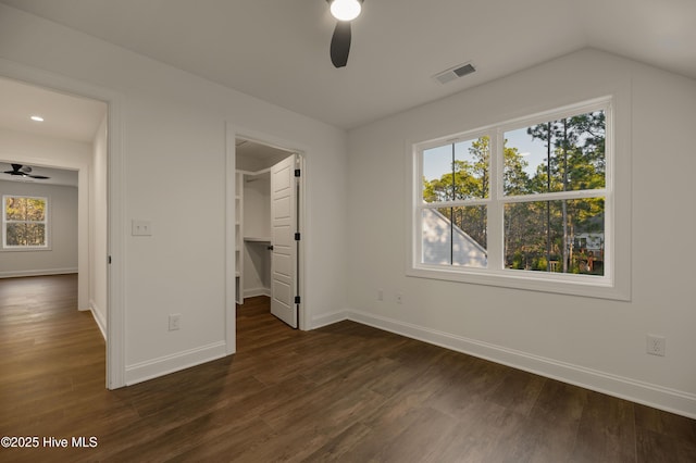 unfurnished bedroom featuring ceiling fan, a walk in closet, vaulted ceiling, and dark hardwood / wood-style flooring