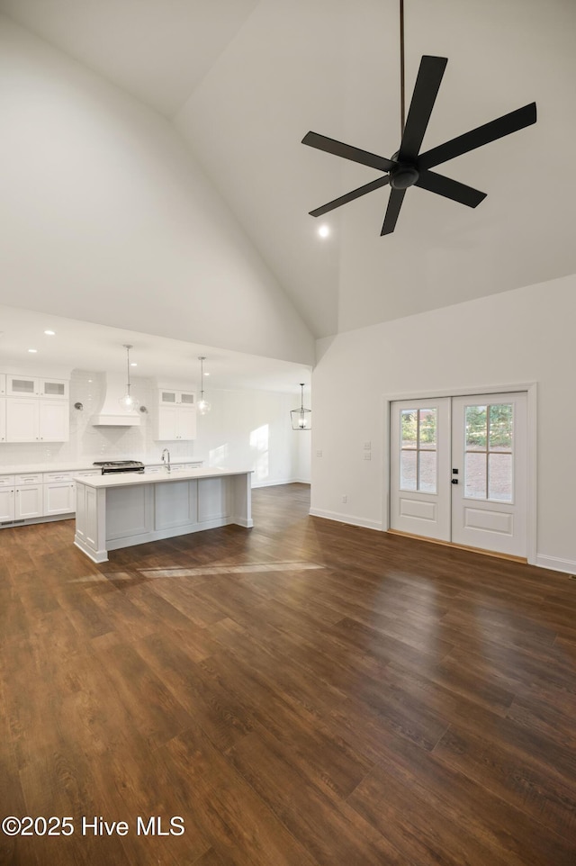 unfurnished living room featuring high vaulted ceiling, dark hardwood / wood-style flooring, and ceiling fan with notable chandelier