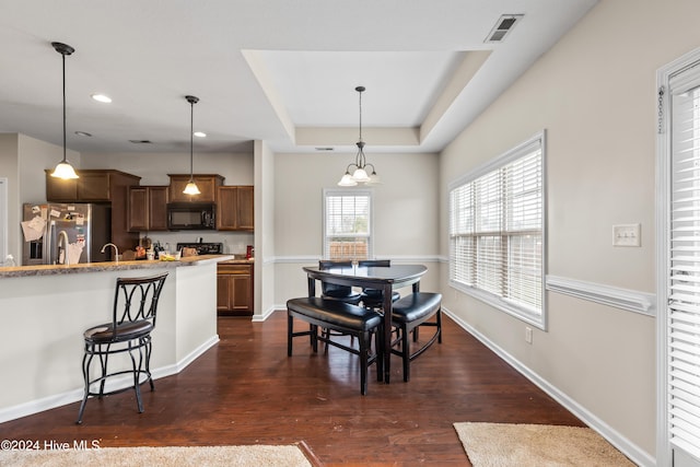 dining space featuring dark hardwood / wood-style flooring, a raised ceiling, and an inviting chandelier