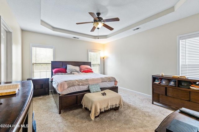 carpeted bedroom with ceiling fan and a tray ceiling