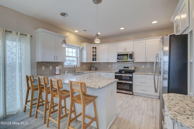 kitchen with decorative backsplash, appliances with stainless steel finishes, decorative light fixtures, light hardwood / wood-style floors, and white cabinetry