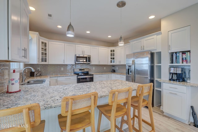 kitchen featuring pendant lighting, a breakfast bar area, light stone countertops, white cabinetry, and stainless steel appliances